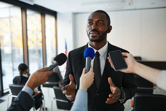 Confident businessman answering questions from the media during a press conference indoors. Corporate communications: a practical guide for 2027