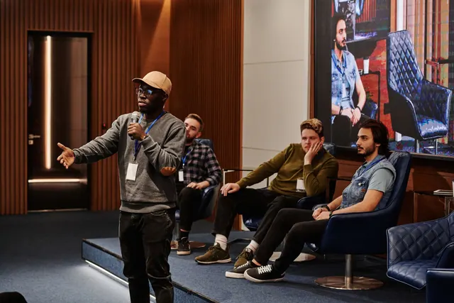 A group of diverse men engaging in a business conference with a speaker holding a microphone. Marketing communications strategy development, one decision at a time