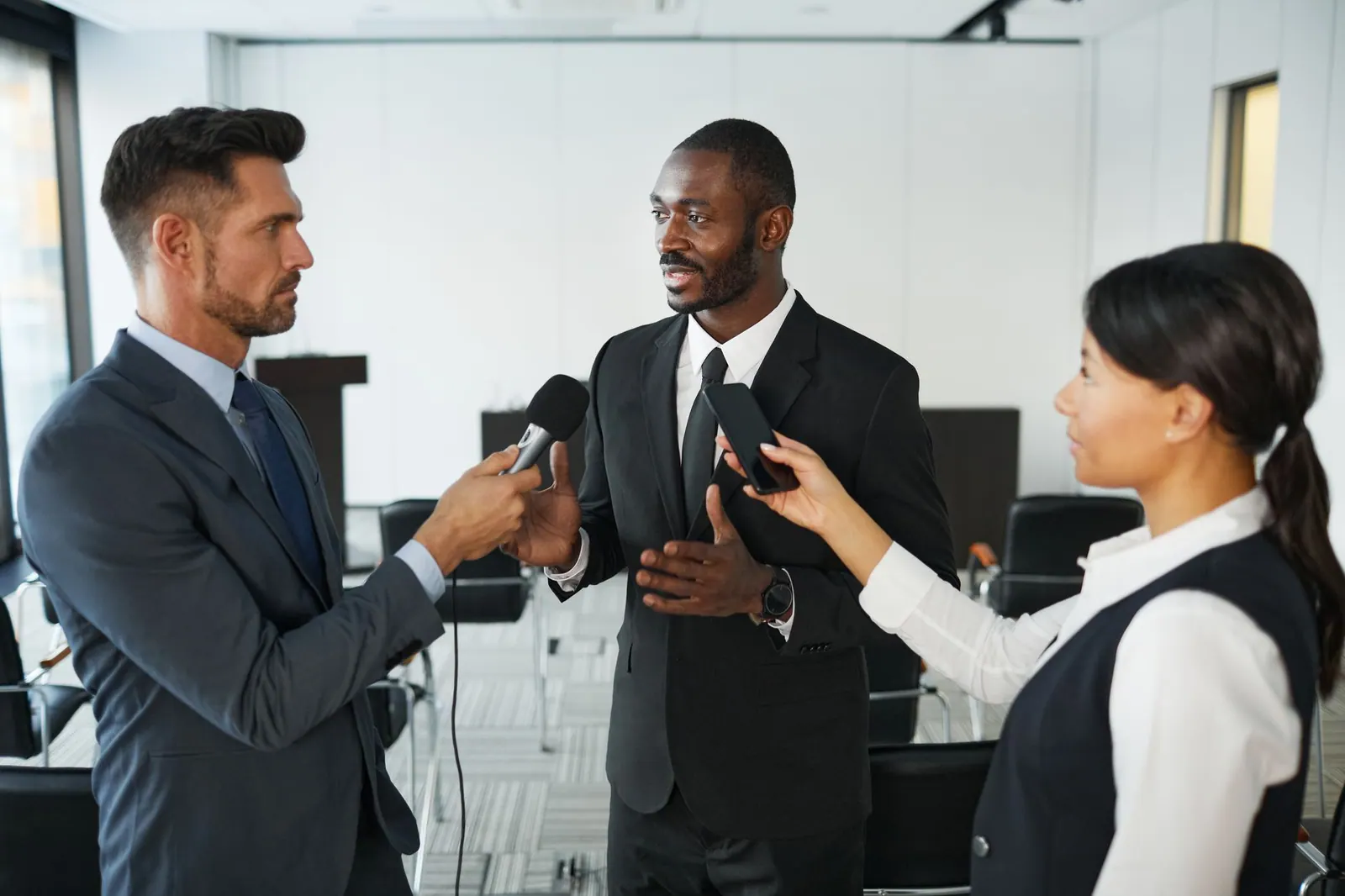 African American businessman in formal attire being interviewed by journalists with microphones in a conference room. Diagnosing the failure pattern in a marketing communications strategy