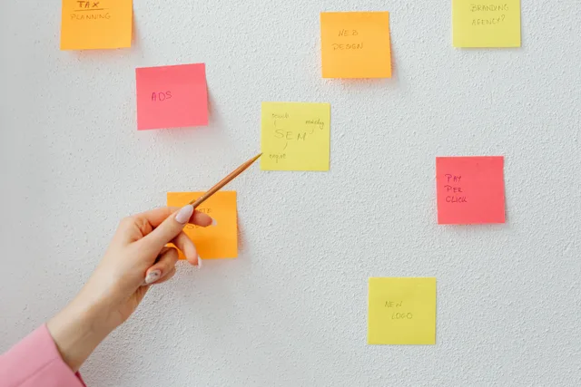 Hand pointing at colorful sticky notes with business concepts on a wall. Public relations strategy best practices for clear messaging