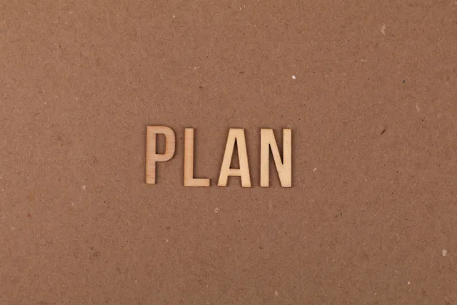 Wooden letters spelling 'PLAN' on a textured cardboard background with ample copy space. Planning template for public relations strategy development